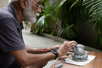 Indian old man crafting an eco-friendly clay Ganesh idol for Ganesh Chaturthi and teaching kids how...