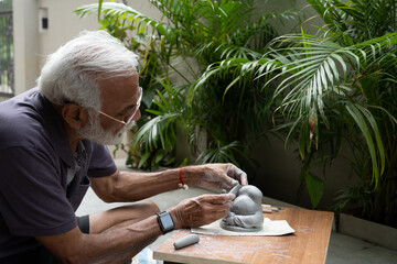 Indian old man crafting an eco-friendly clay Ganesh idol for Ganesh Chaturthi and teaching kids how...