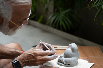 Indian old man crafting an eco-friendly clay Ganesh idol for Ganesh Chaturthi and teaching kids how to do it, sitting outdoors in a garden
