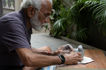 Indian old man crafting an eco-friendly clay Ganesh idol for Ganesh Chaturthi and teaching kids how...