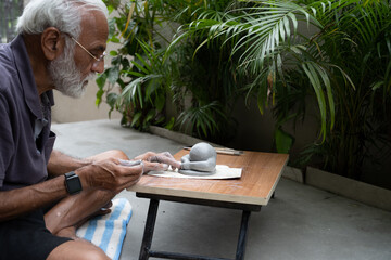 Indian old man crafting an eco-friendly clay Ganesh idol for Ganesh Chaturthi and teaching kids how...