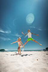 Children leap into summer sky on sunny beach, full body jump frozen mid air. Pure childhood freedom and energy against vivid blue backdrop. Early travel booking