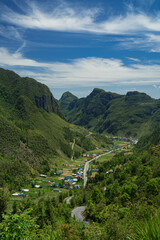 The road winds through the mountain, revealing a scenic landscape where nature meets the sky,...