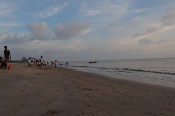 Sunset over calm ocean casting warm glow across the water. Beach sandy under sky is lightly clouded...