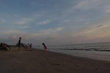 Sunset over calm ocean casting warm glow across the water. Beach sandy under sky is lightly clouded...
