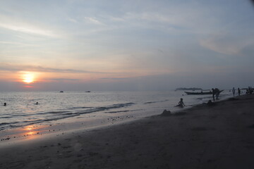 Sunset over calm ocean casting warm glow across the water. Beach sandy under sky is lightly clouded...