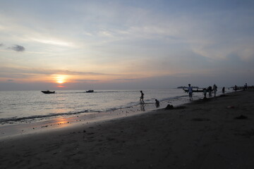 Sunset over calm ocean casting warm glow across the water. Beach sandy under sky is lightly clouded...