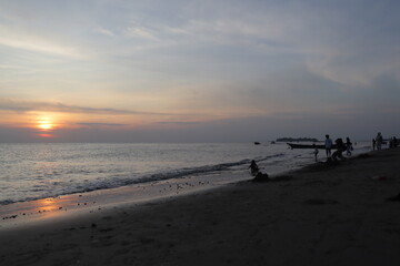Sunset over calm ocean casting warm glow across the water. Beach sandy under sky is lightly clouded...