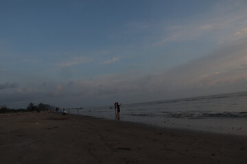 Sunset over calm ocean casting warm glow across the water. Beach sandy under sky is lightly clouded...