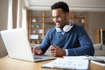 Fototapeta premium Man working from home on laptop computer with headphones and documents on desk happy face