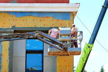 Exterior wall insulation with mineral wool cladding and plaster coating, workers operate from crane...