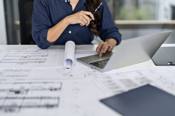 Female Asian engineer organizing blueprints for projects in office workspace