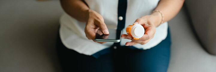 Female Asian reading drug information on smartphone with pill bottle