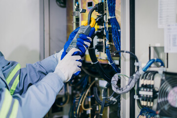Electrician engineer worker testing electric cable at main power line cabinet fuse box.