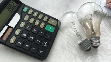 Two incandescent lamps are lying on the table, a woman is writing down the price, the electricity bill. The rise in price of electricity. Economy. - Powered by Adobe