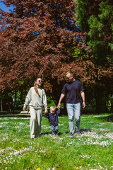Fototapeta premium On a sunny day, a happy family of four enjoys time together in a vibrant park, sharing laughter, playing games, and making memories amidst the beautiful nature and blooming flowers