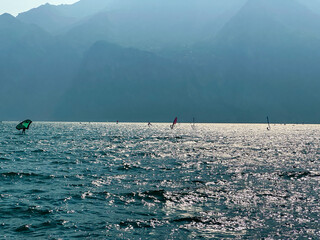Windsurfers and foilers enjoy the strong wind on the choppy waters of Lake Garda, framed by the...