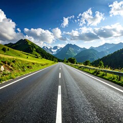 Fototapeta premium A paved road stretches into a vista of verdant hills and towering mountains under a vibrant blue sky filled with fluffy clouds.