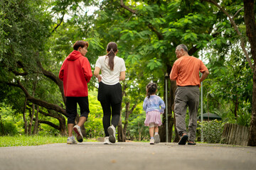 Fototapeta premium Asian family jogging together in the park. Parents, child, and grandfather exercising outdoors