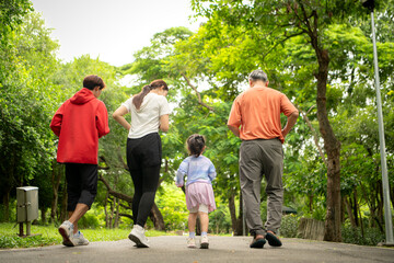 Fototapeta premium Asian family jogging together in the park. Parents, child, and grandfather exercising outdoors