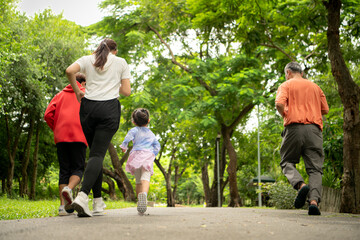 Obraz premium Asian family jogging together in the park. Parents, child, and grandfather exercising outdoors