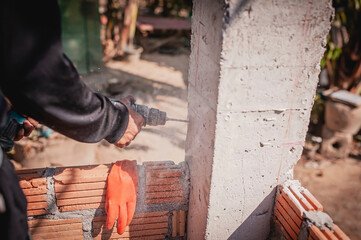 A technician uses a drill to drill a post to strengthen the adhesion of the brick wall.