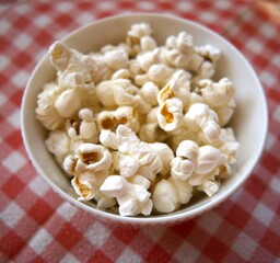Fresh popcorn in a white bowl placed on a red checkered napkin with copy space.