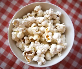 Fresh popcorn in a white bowl placed on a red checkered napkin with copy space.