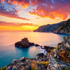 A vibrant sunrise paints the coastal landscape with fiery hues, showcasing a tranquil bay nestled between dramatic rocky cliffs.