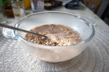 Chocolate flavored oatmeal powder prepared with water in a clear glass bowl, close-up.