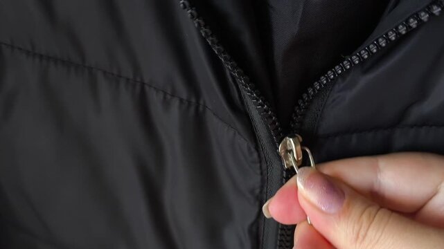 A woman's hands fasten the zip of a black jacket. A warm winter jacket with a sintepon.