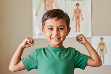 Portrait of Caucasian boy child smiling and flexing arms in front of anatomical posters, showing confidence and happiness, looking directly at camera in medical setting