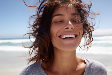 A woman with long brown hair is smiling and looking out at the ocean