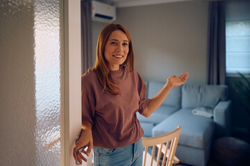 Happy woman inviting guests in her new house and looking at camera.