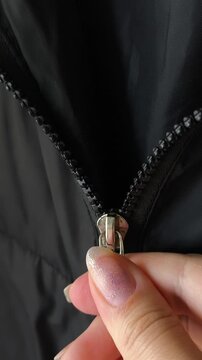 A woman's hands fasten the zip of a black jacket. A warm winter jacket with a sintepon.