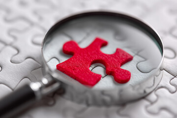 A magnifying glass is used to look at a red puzzle piece
