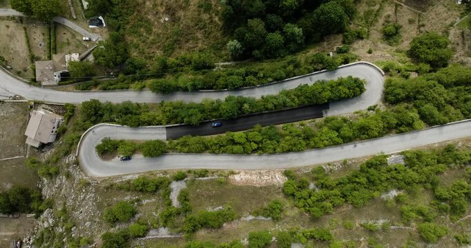 Aerial view of winding road cutting through lush green landscape with cars, contrasting with the gray asphalt, Scanno, Abruzzo, Italy.