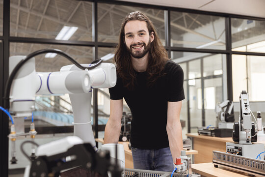 Portrait happy smile engineer male learning education in Industrial Robotics program with robot arm simulation model in university engineering lab classroom.