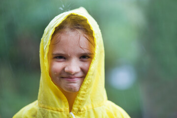 A smiling little girl in a yellow raincoat stands in the rain 