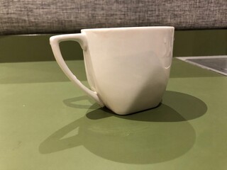 White ceramic mug sitting on a green table casting a shadow