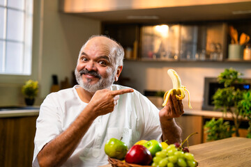 Fototapeta premium Indian Old man eating banana in kitchen, focused on healthy lifestyle and wellness