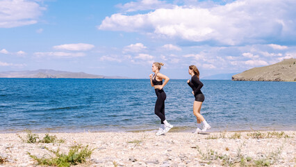Two women running on beach during cardio training session by water
