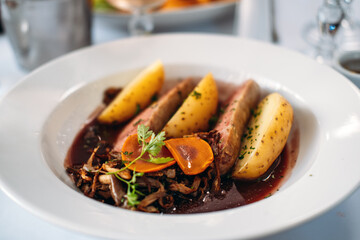 Traditional Lyonnais sausage served with steamed potatoes, wild mushrooms, and red sauce in a white bowl. Regional cuisine, nose-to-tail cooking, sustainable food practices, French culinary heritage