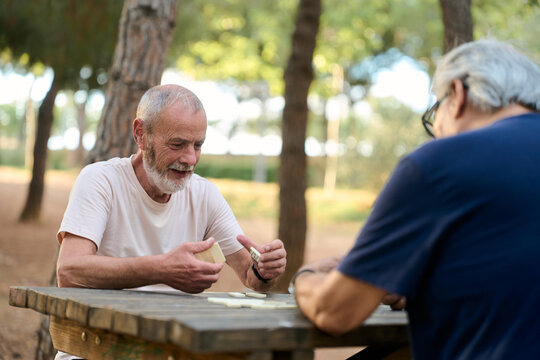 Two senior men playing dominoes in park, enjoying retirement - Powered by Adobe