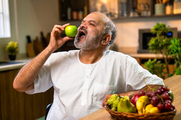 Fototapeta premium Old Indian man eating green apple indoors as part of his morning wellness routine