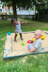 Two young children joyfully playing together in a colorful sandbox at a lively park during a...