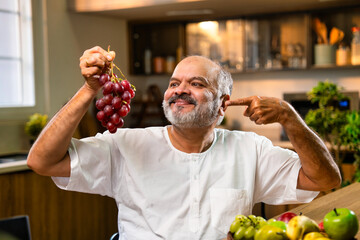 Indian Old man eating grapes for health in cozy modern Indian kitchen