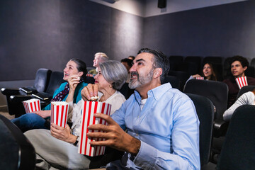 Group of diverse people enjoying a movie and eating popcorn in a comfortable cinema, experiencing the joy of shared entertainment