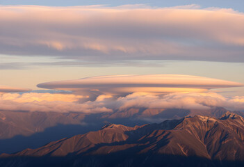 Naklejka premium Unusual lenticular cloud formation over mountain range at sunrise.