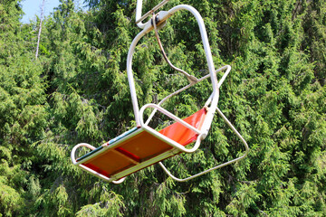 An empty ski lift chair stands out with a bright orange back against the background of a dense...